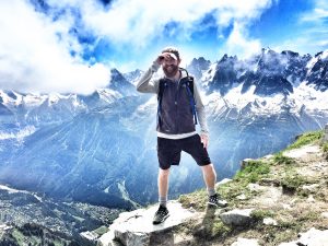 man standing on cliff with mountains behind him
